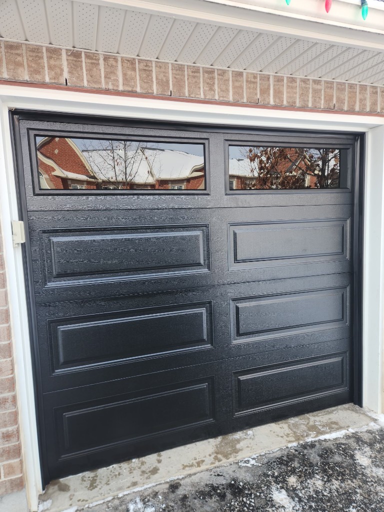 Black insulated garage door with windows on a brick Ottawa home in winter